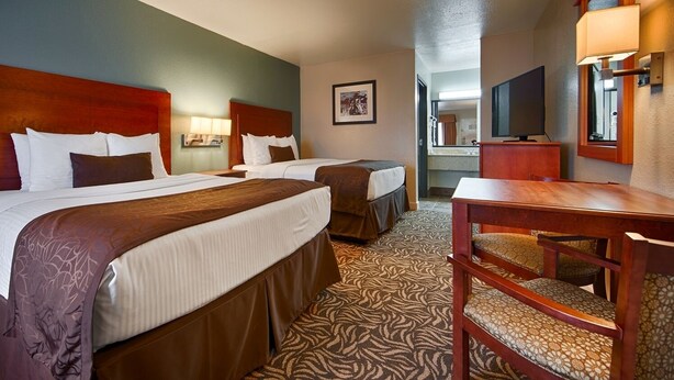A hotel room with two beds, a desk, a chair, a television, and a mirror. - Best Western Regency Inn & Suites (Gonzales)
