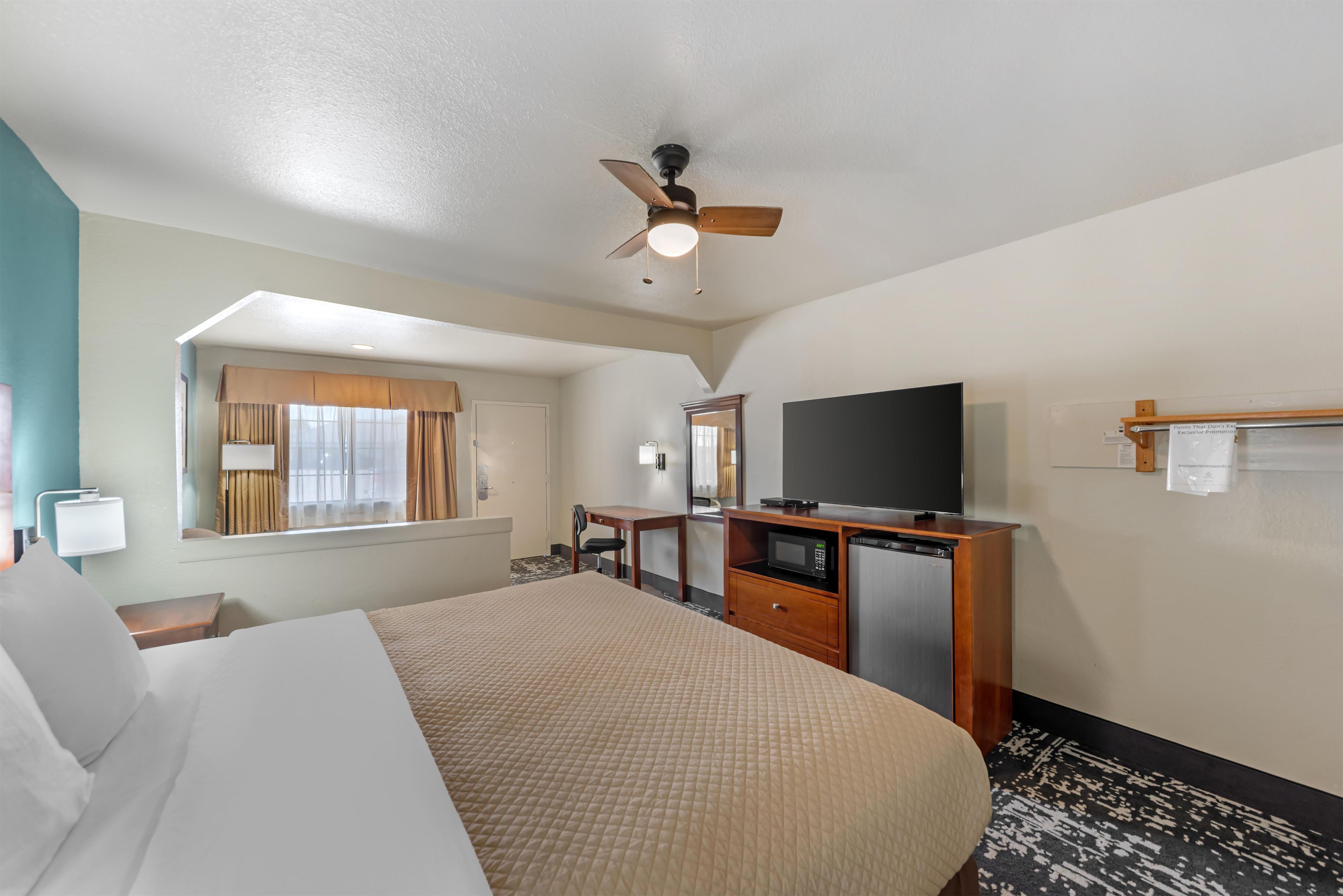 A hotel room with a bed, a desk with a television, a microwave, and a ceiling fan.