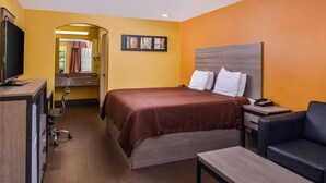 A hotel room with a bed, a desk, a chair, a TV, and a bathroom with a mirror and shower. - Americas Best Value Inn West Columbia (West Columbia)