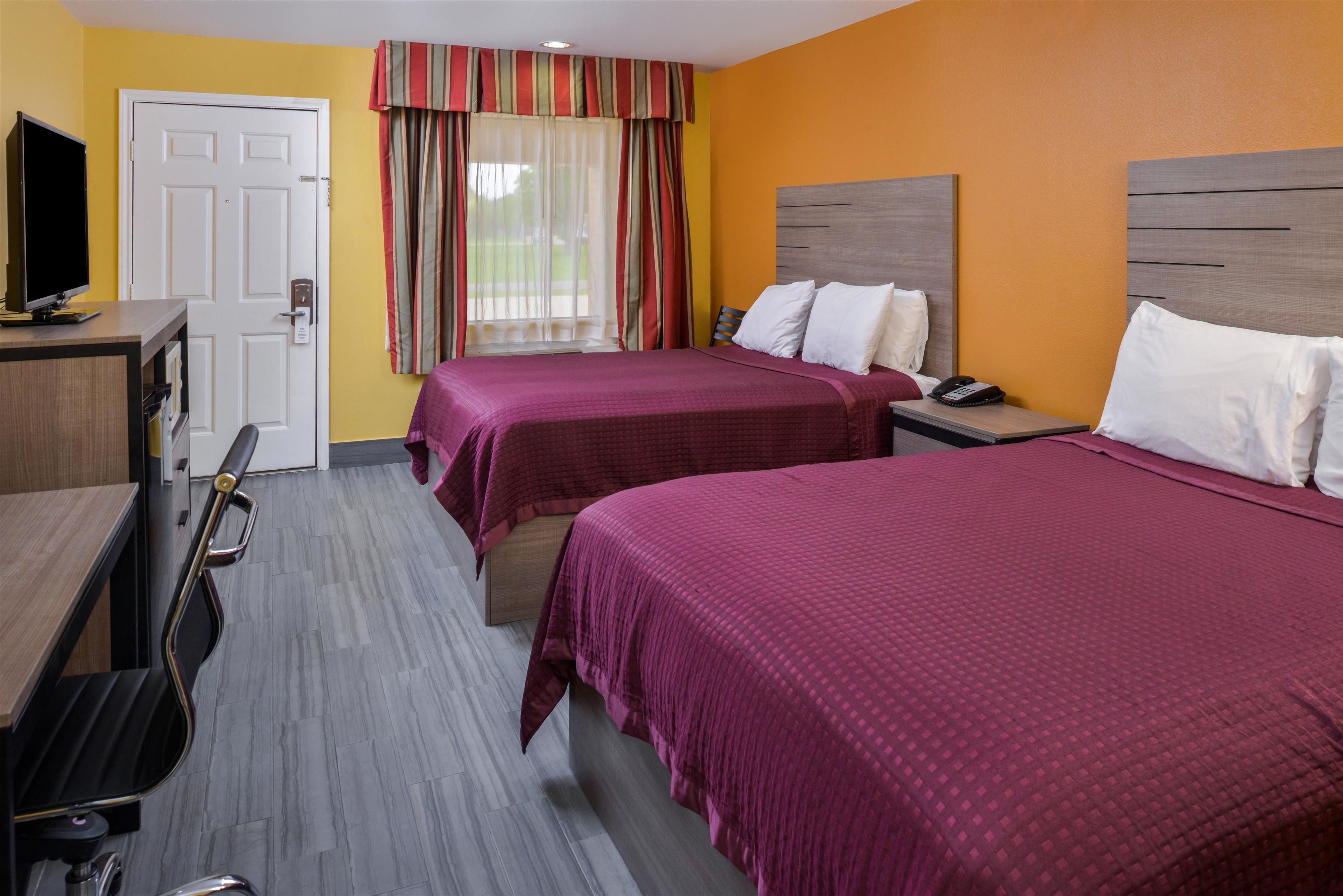 A hotel room with two beds, a desk with a computer, a TV, and a door.