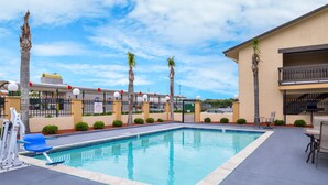 A rectangular swimming pool with a tiled edge, surrounded by a low wall and palm trees. - Americas Best Value Inn West Columbia (West Columbia)