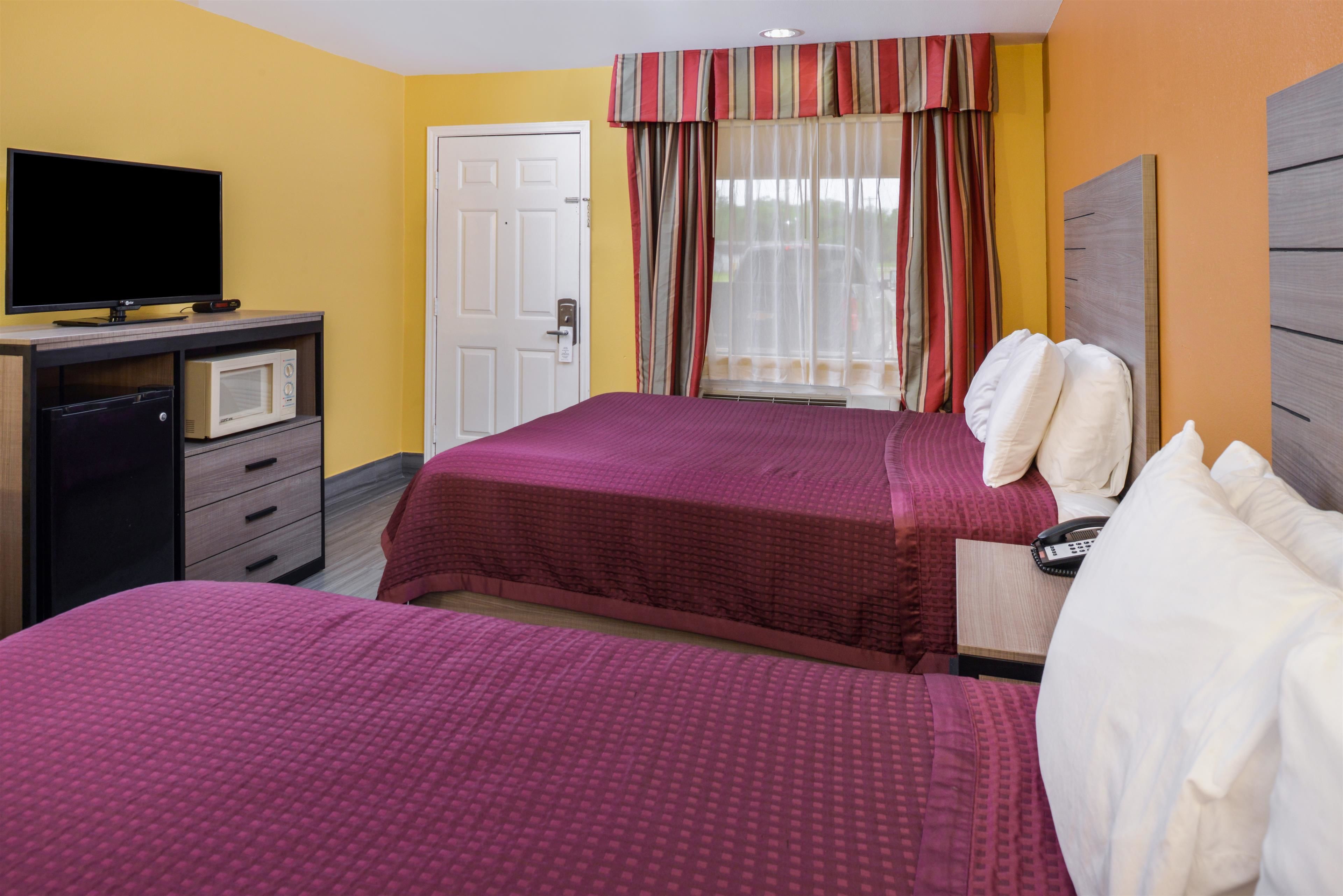 Quarto de hotel com duas camas, televisão, micro-ondas e porta.
