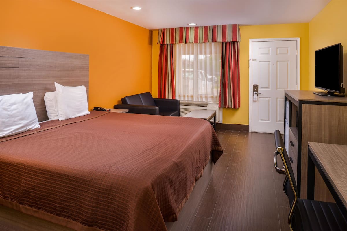 A hotel room with a large bed, a desk with a television, a chair, and a door.