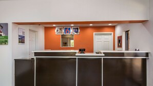 En receptionsdisk med en vit bardisk och en orange vägg, en dörr till vänster och en dörr till höger.
