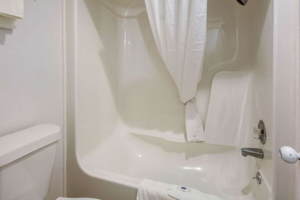 Una bañera blanca con cortina de ducha, una toalla y dispensador de jabón.