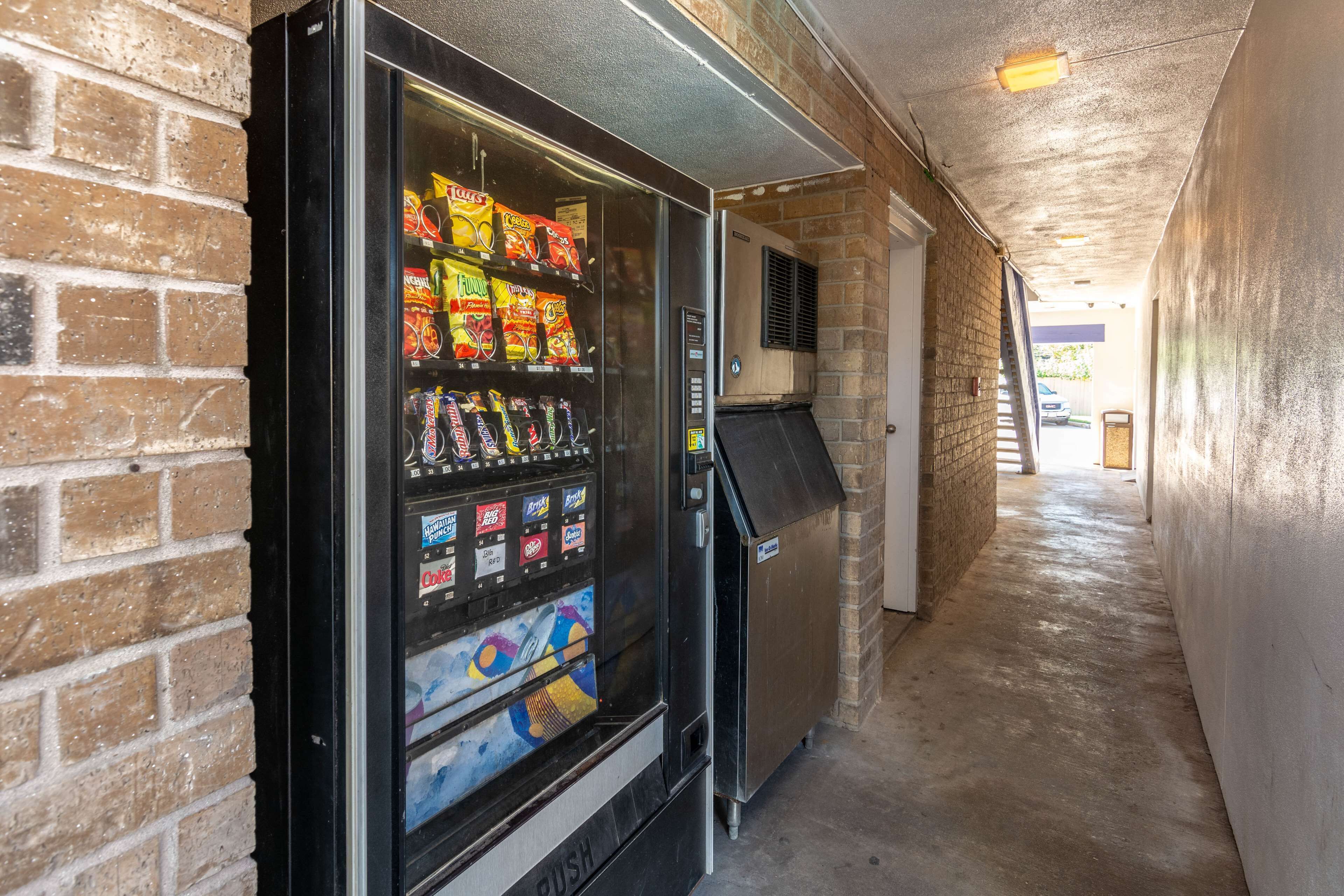A vending machine with snacks and beverages, located in a narrow hallway with brick walls and a concrete floor.