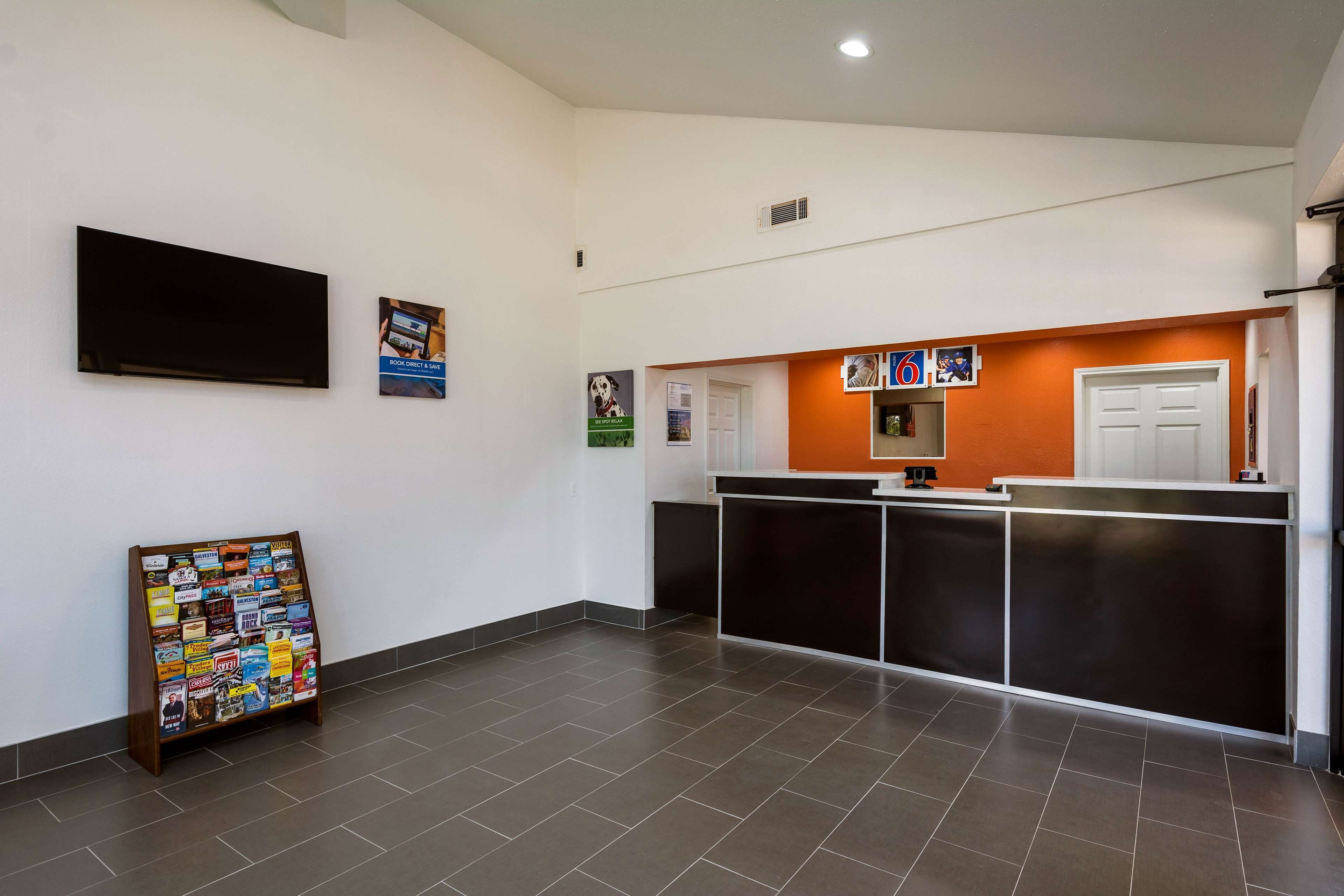 A reception area with a black reception desk, a bulletin board with various notices, and a wall-mounted TV.