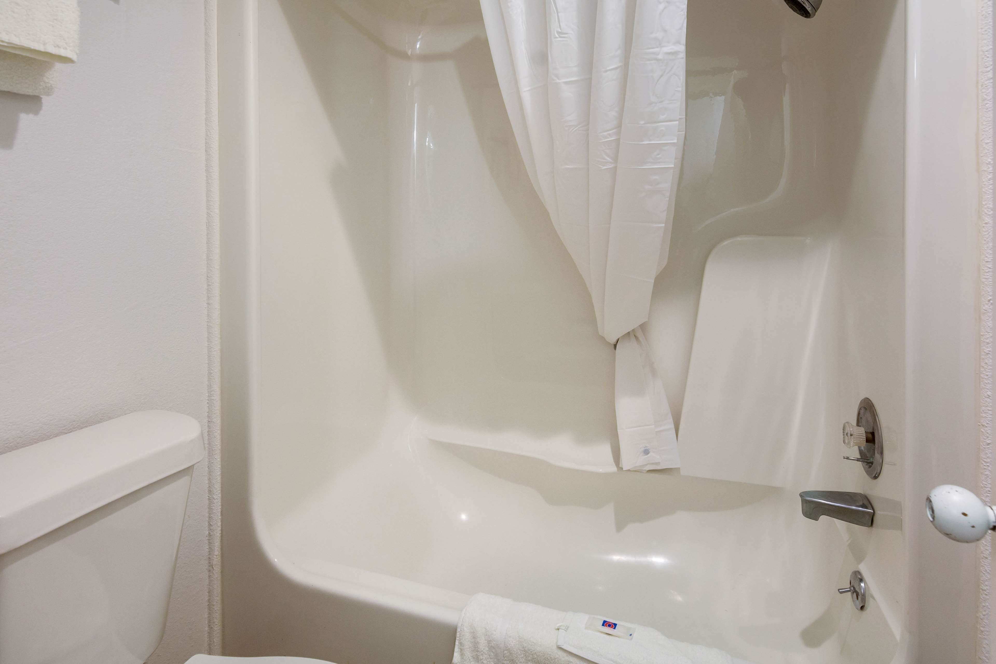 Eine weiße Badewanne mit Duschvorhang, ein Handtuch und eine Toilette in der Ecke.