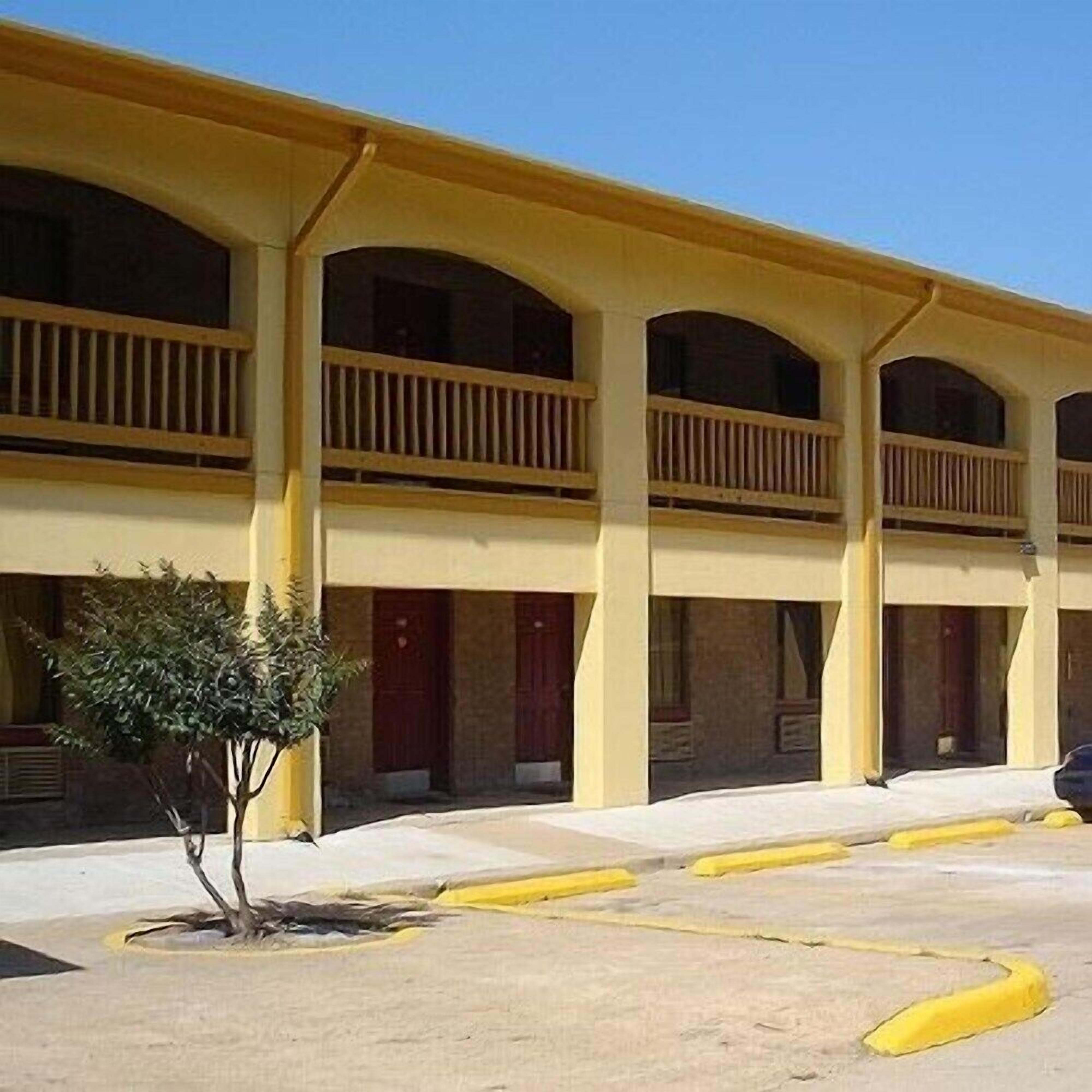 A building with a yellow facade, multiple balconies, and a parking area with yellow curbs.