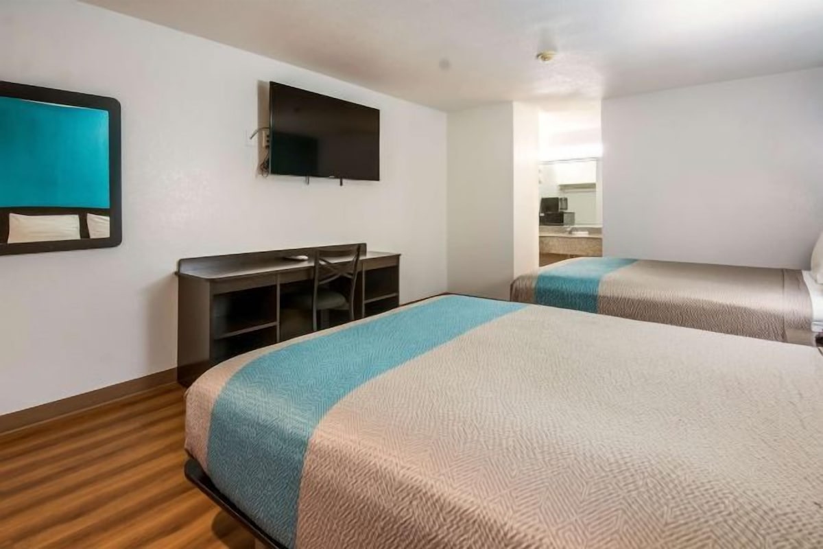 Habitación de hotel con dos camas, un escritorio y una televisión.