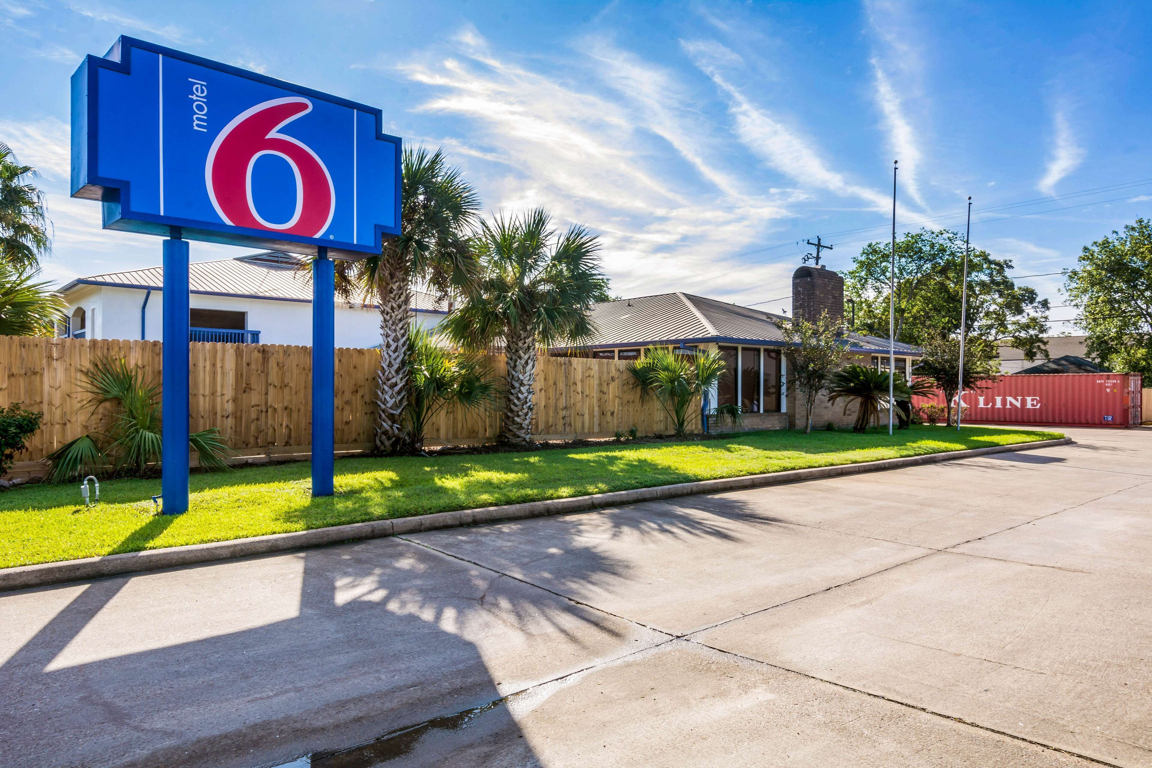 A motel sign with the number 6, a wooden fence, and a building with a sloped roof.