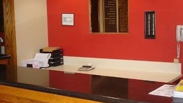 Un mostrador de recepción con una pared roja, un certificado enmarcado y un teléfono.
