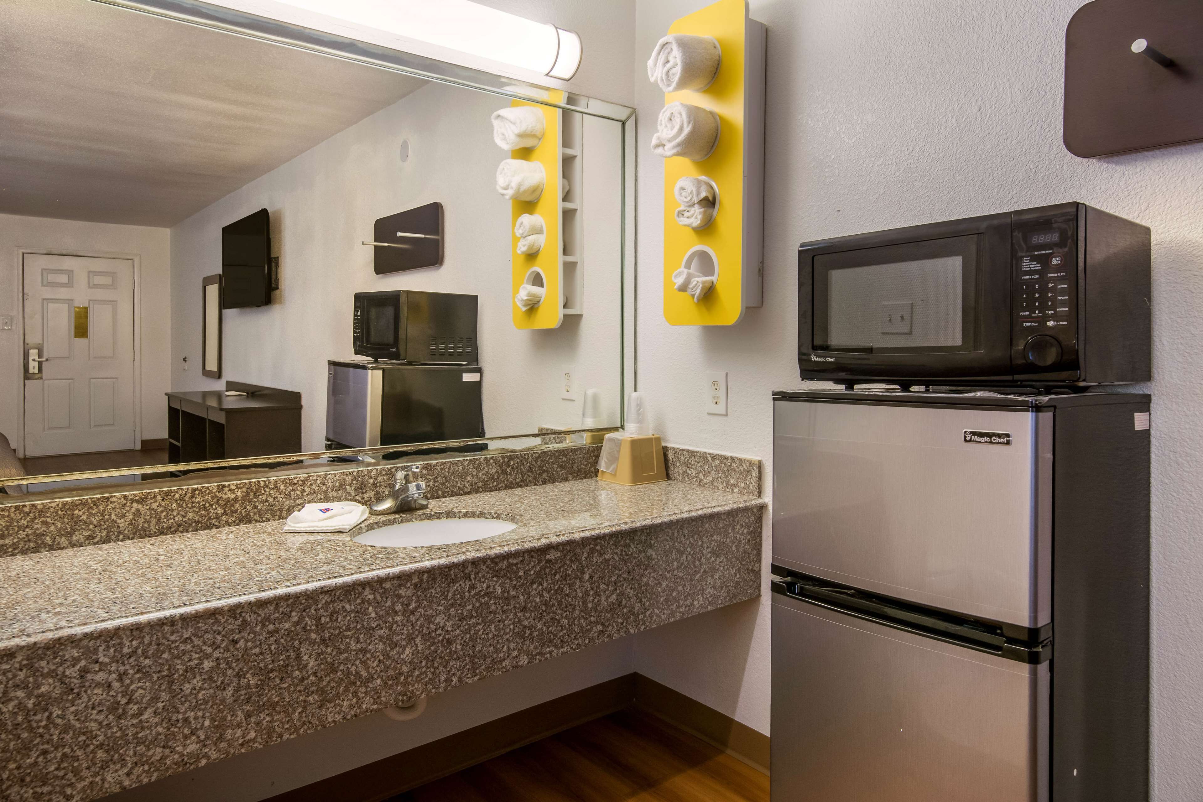 A hotel bathroom with a granite countertop sink, a mirror, a microwave, and a refrigerator.