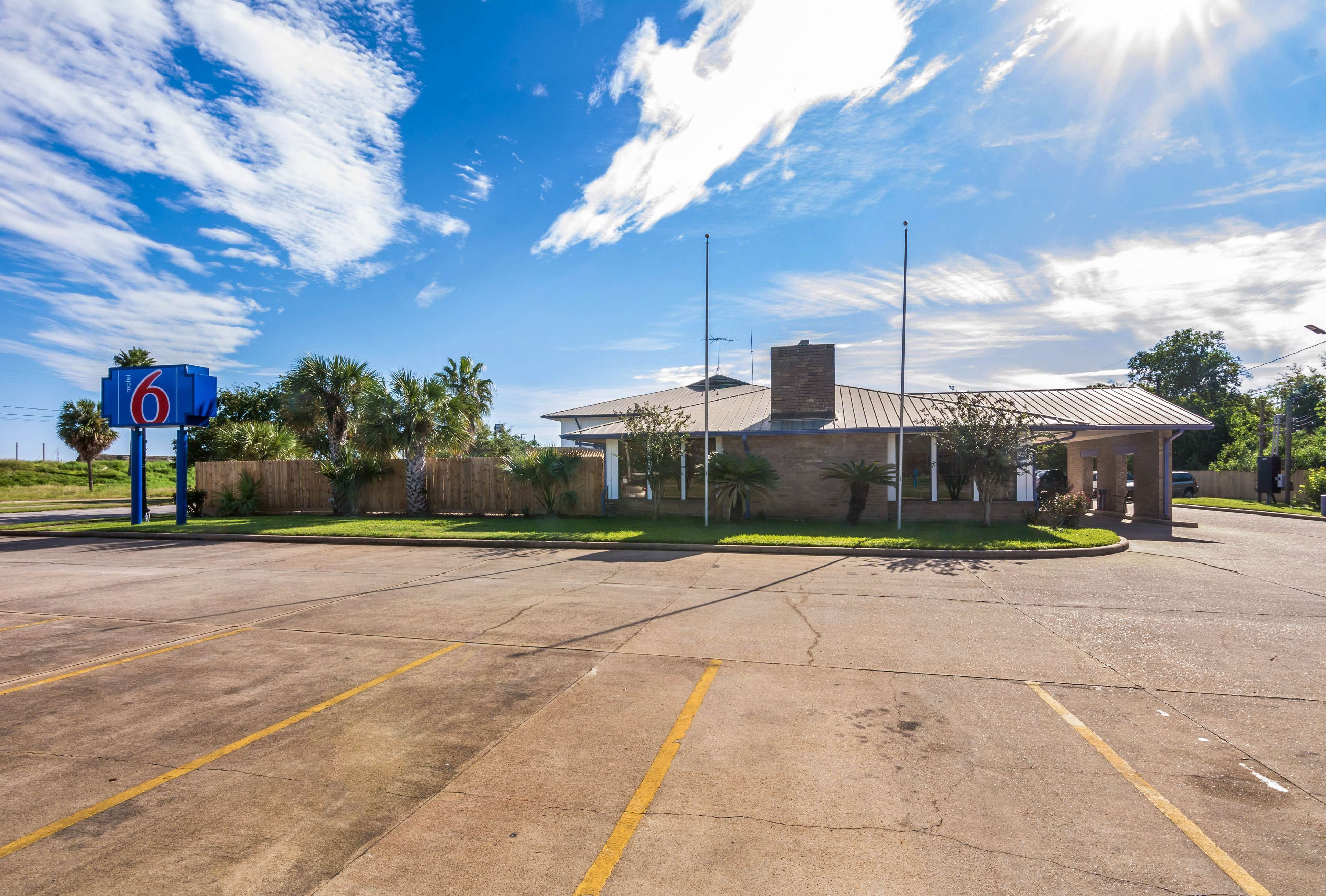 A parking lot with a motel sign, a building with a metal roof, and palm trees.