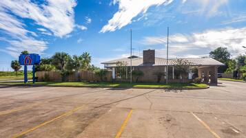 A parking lot with a motel sign, a building with a metal roof, and palm trees.