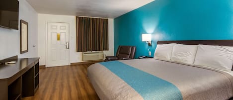 A hotel room with a bed, a desk, a chair, a TV, and a door.