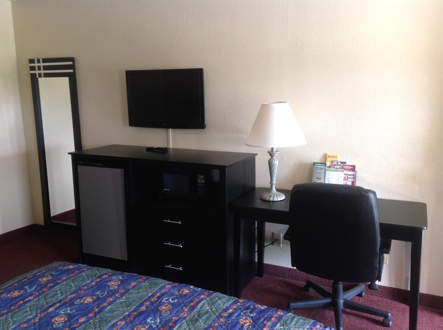 A hotel room with a bed, a desk, a chair, a television, a lamp, and a mirror.