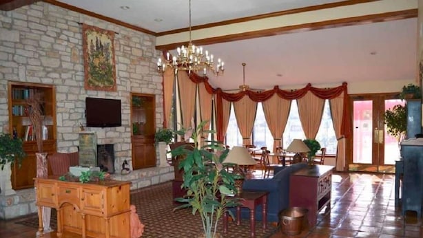 A spacious living room with a stone fireplace, wooden furniture, and large windows with red curtains.