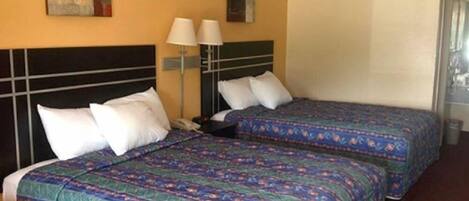 A hotel room with two beds, each with a patterned bedspread, a nightstand with a lamp, and artwork on the walls.