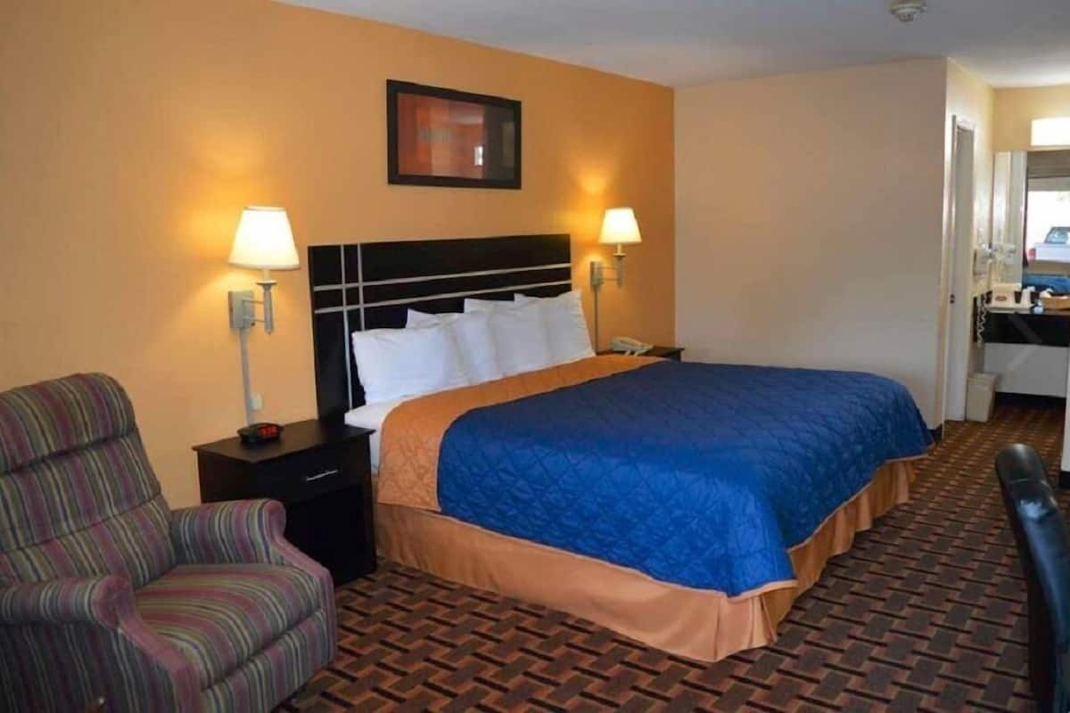 Een hotelkamer met een groot bed, twee bedlampen, een gestreept fauteuil, een nachtkastje en een klein tafeltje met een telefoon.