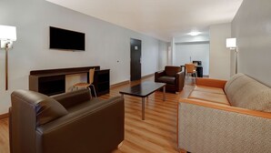 Una sala de estar moderna con sofá, sillón y mesa de centro. Hay un televisor de pantalla plana montado en la pared, una puerta y una pequeña mesa con sillas.