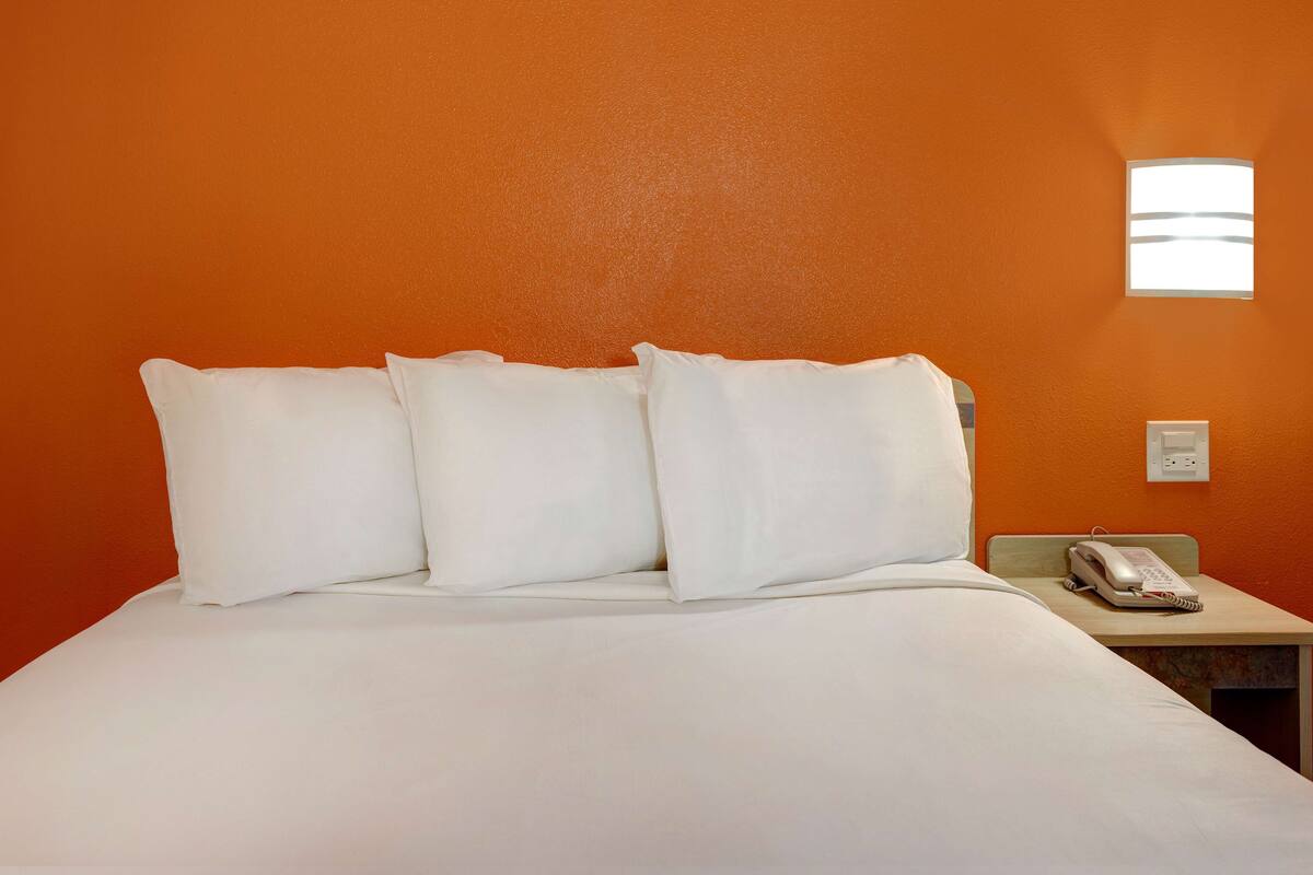 Een hotelkamer met een oranje wand, een bed met wit beddengoed en een telefoon op het nachtkastje.