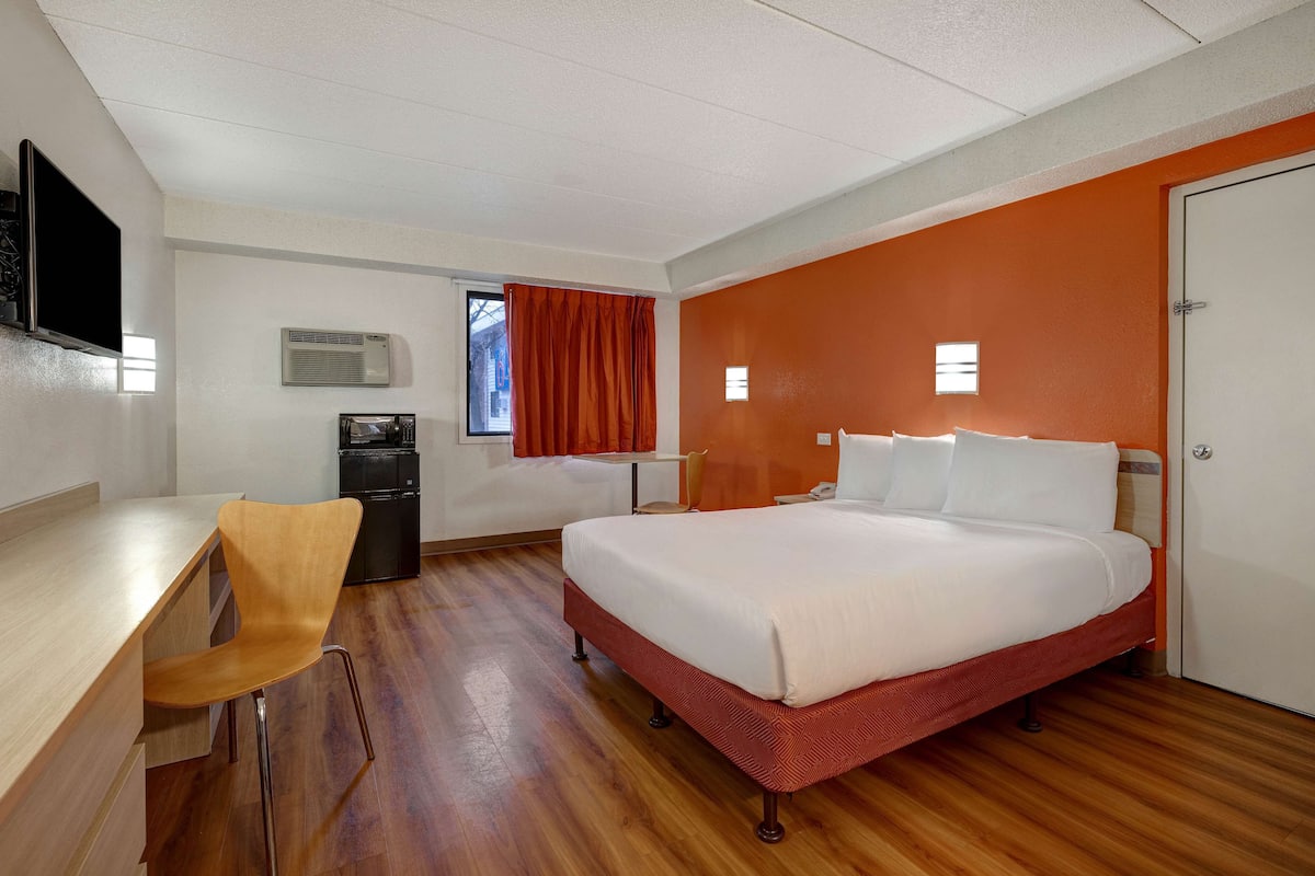 Een hotelkamer met een bed, een bureau, een stoel, een televisie, een magnetron en een airconditioning.