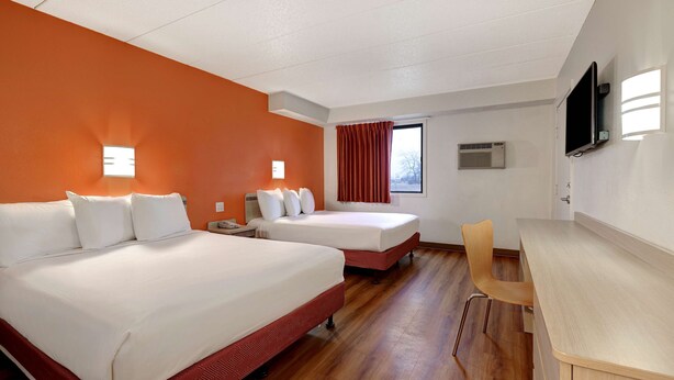 Habitación de hotel con dos camas, un escritorio, una silla, un televisor y una ventana con cortinas.