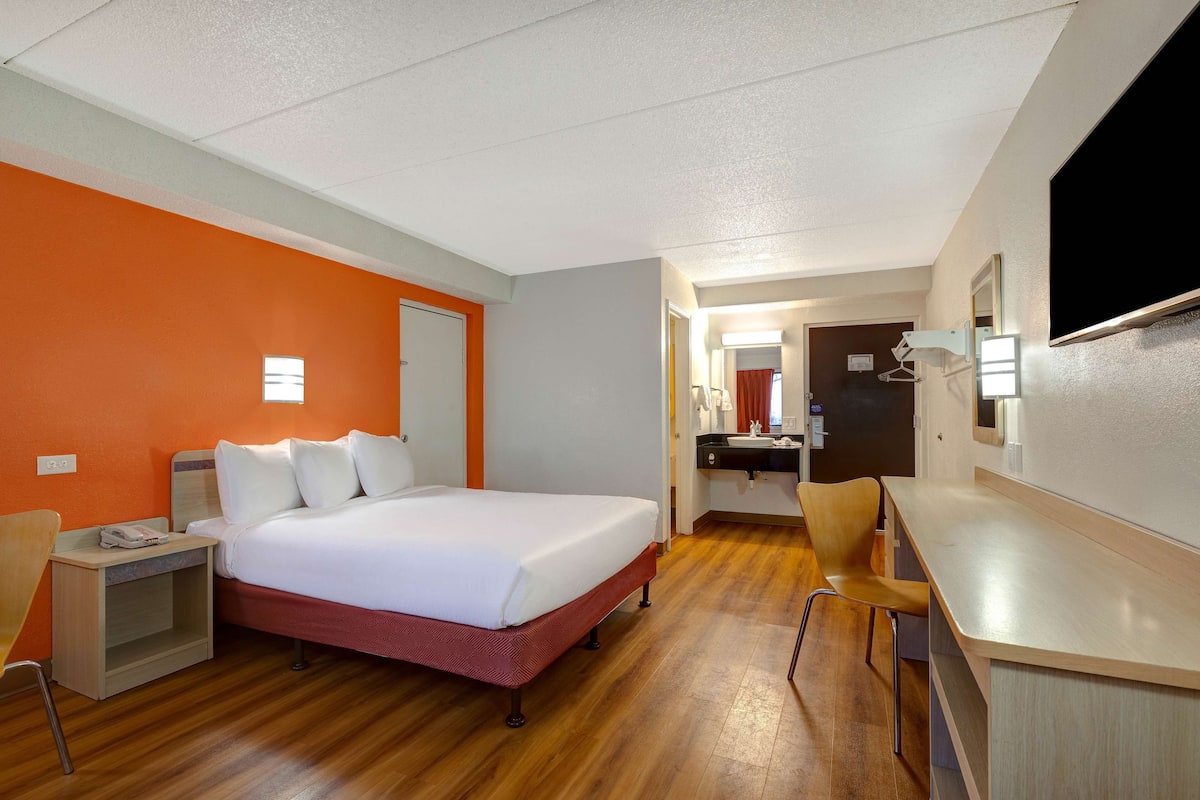 Een hotelkamer met een bed, een bureau, een stoel, een spiegel en een televisie.