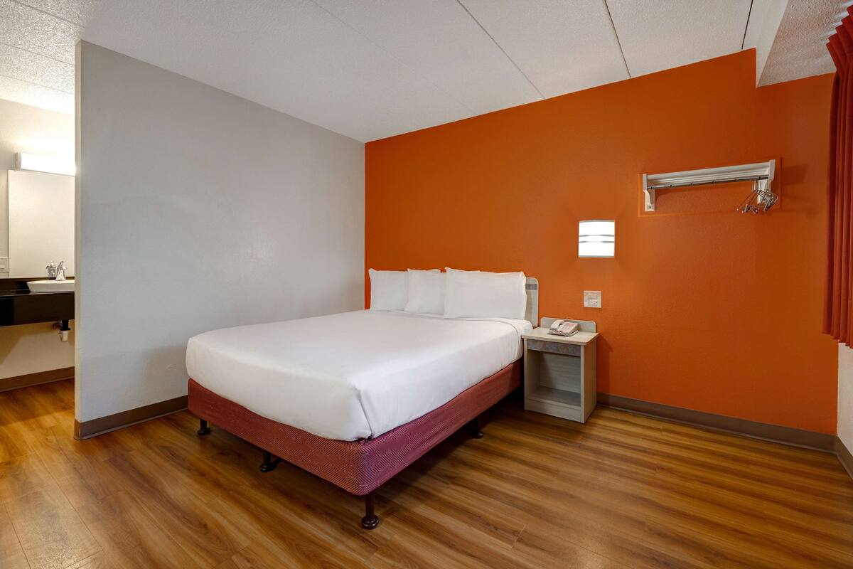 Een hotelkamer met een groot bed, een nachtkastje met een lamp en een wandairconditioner.