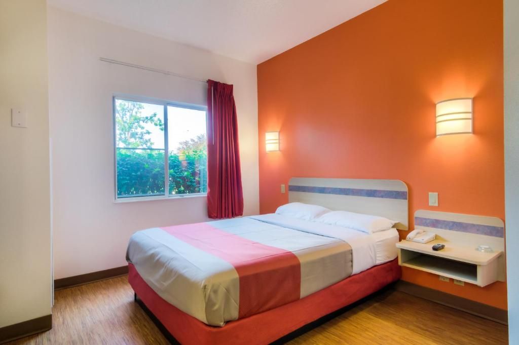 Une chambre d’hôtel avec un lit, une fenêtre avec des rideaux, une table de chevet et des lampes fixées au mur.