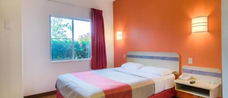 A hotel room with a bed, a window with curtains, a nightstand, and wall-mounted lights.