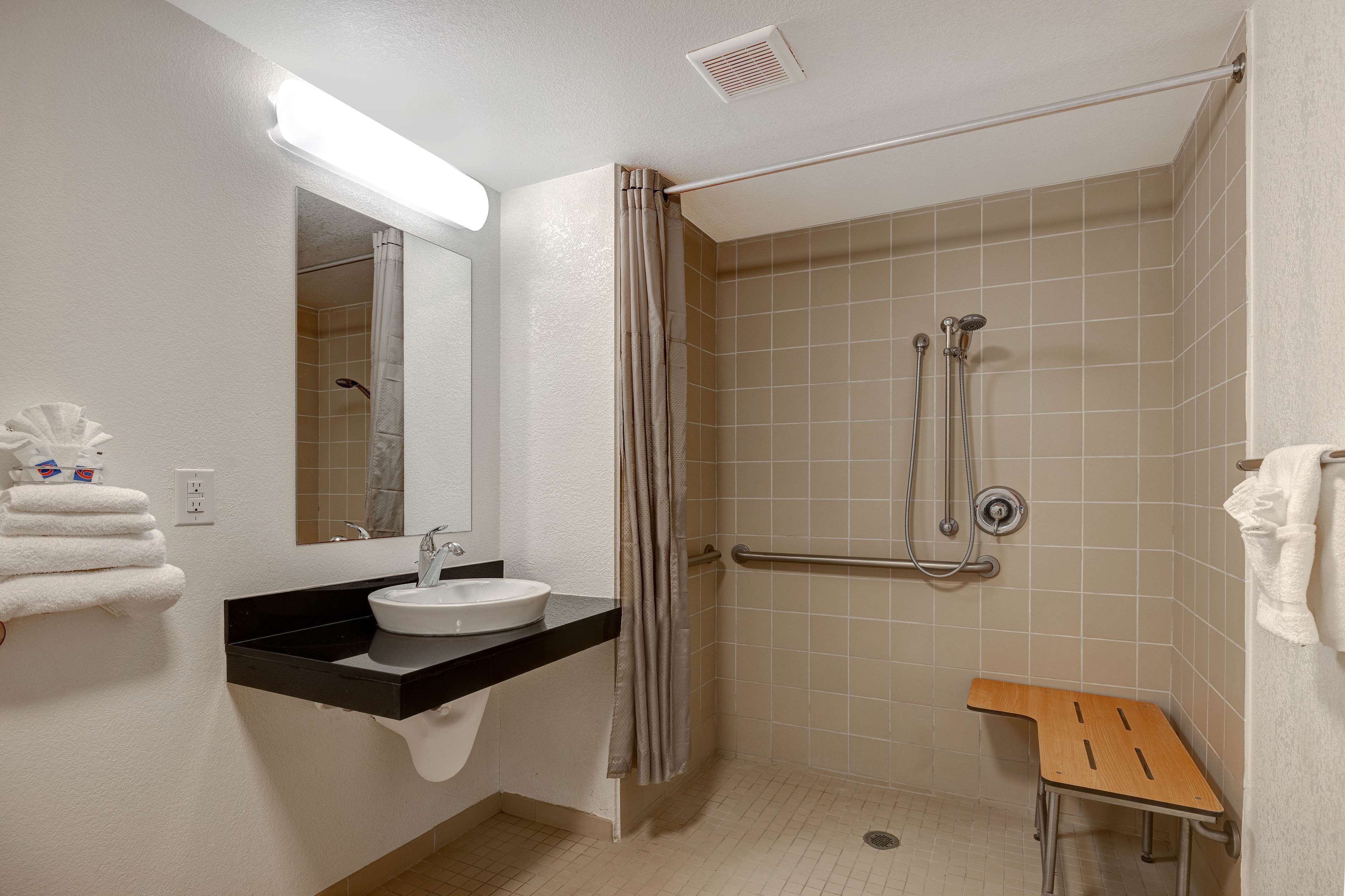 A bathroom with a sink, mirror, shower, and a wooden bench.
