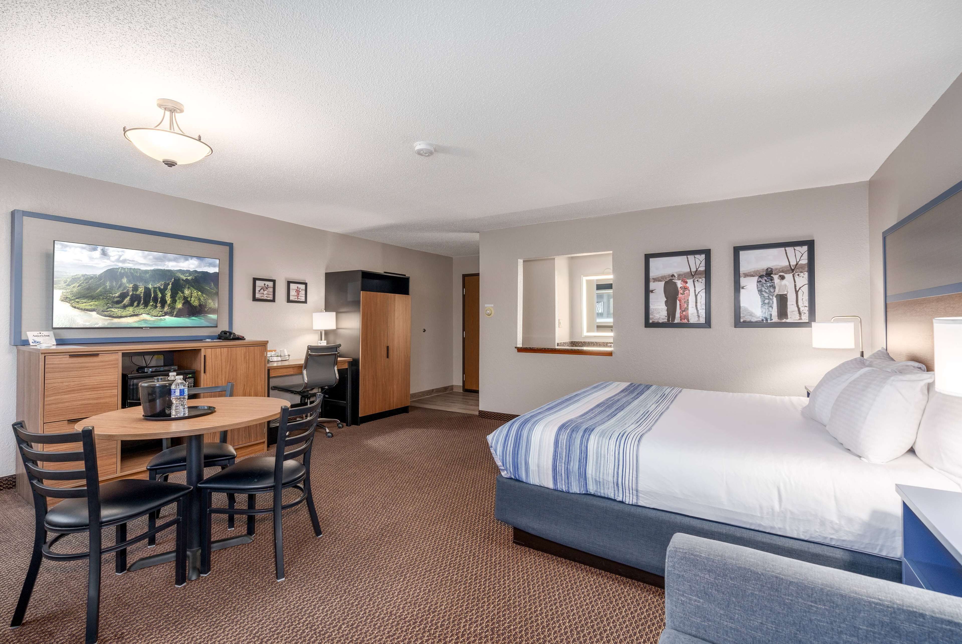 A hotel room with a bed, a desk with a chair, a television, and a small kitchenette.