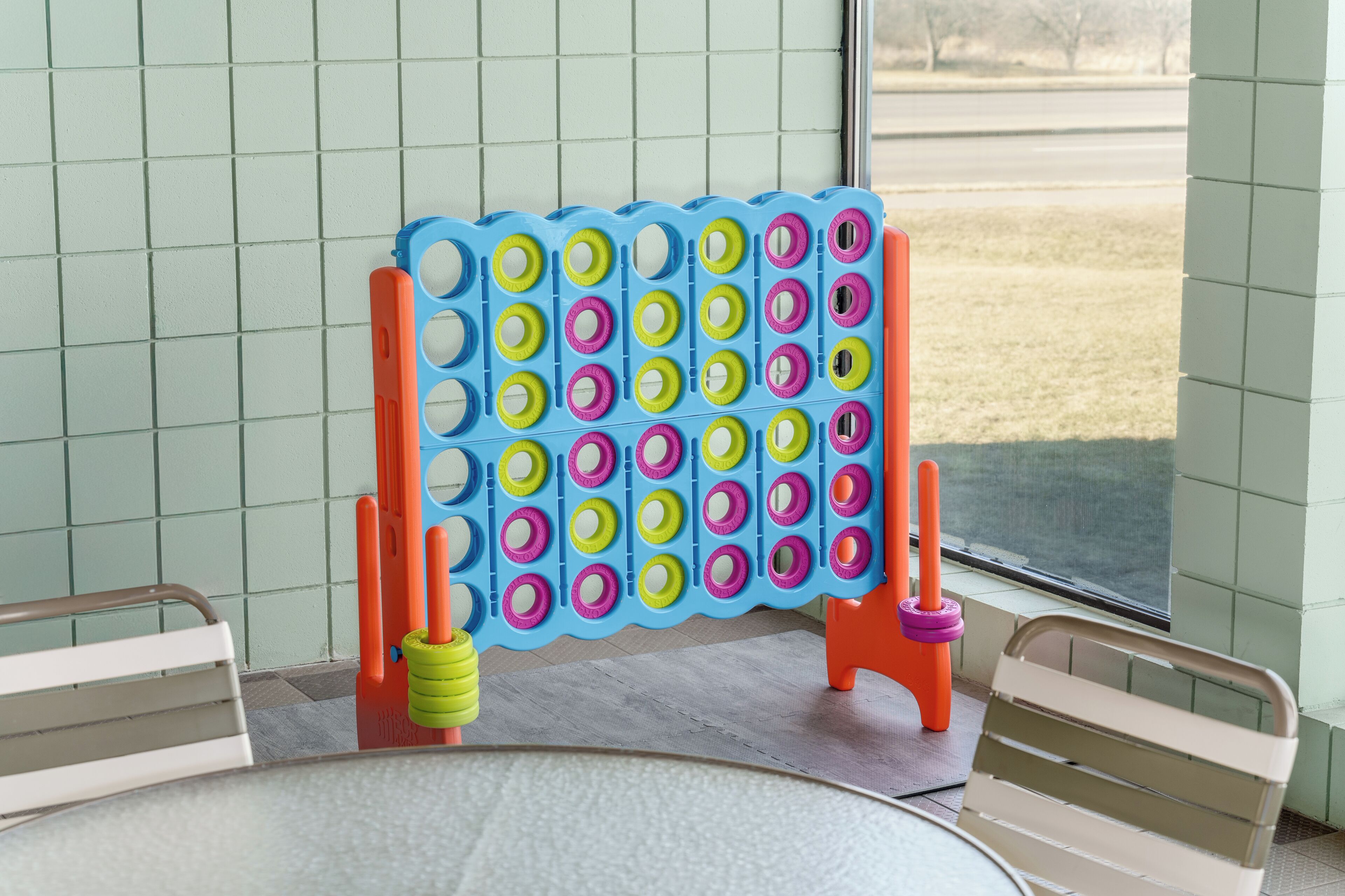 Una mesa con un juego de aros de colores dispuesto frente a una ventana que da a una carretera y árboles.