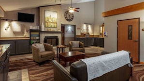 Un vestíbulo de hotel con chimenea, zona de estar, cocina y un reloj en la pared.