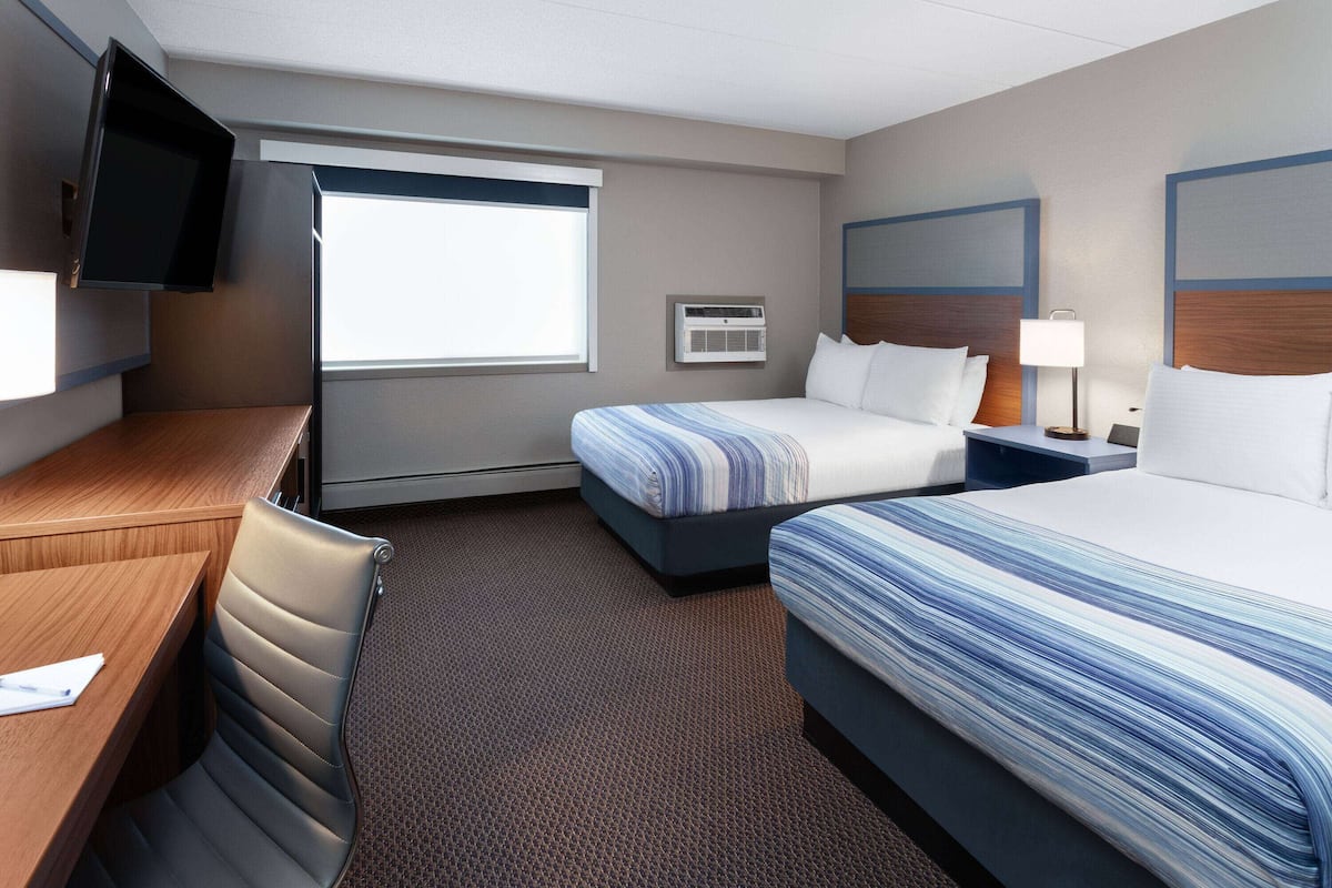 A hotel room with a desk, two beds, a TV, and a window.