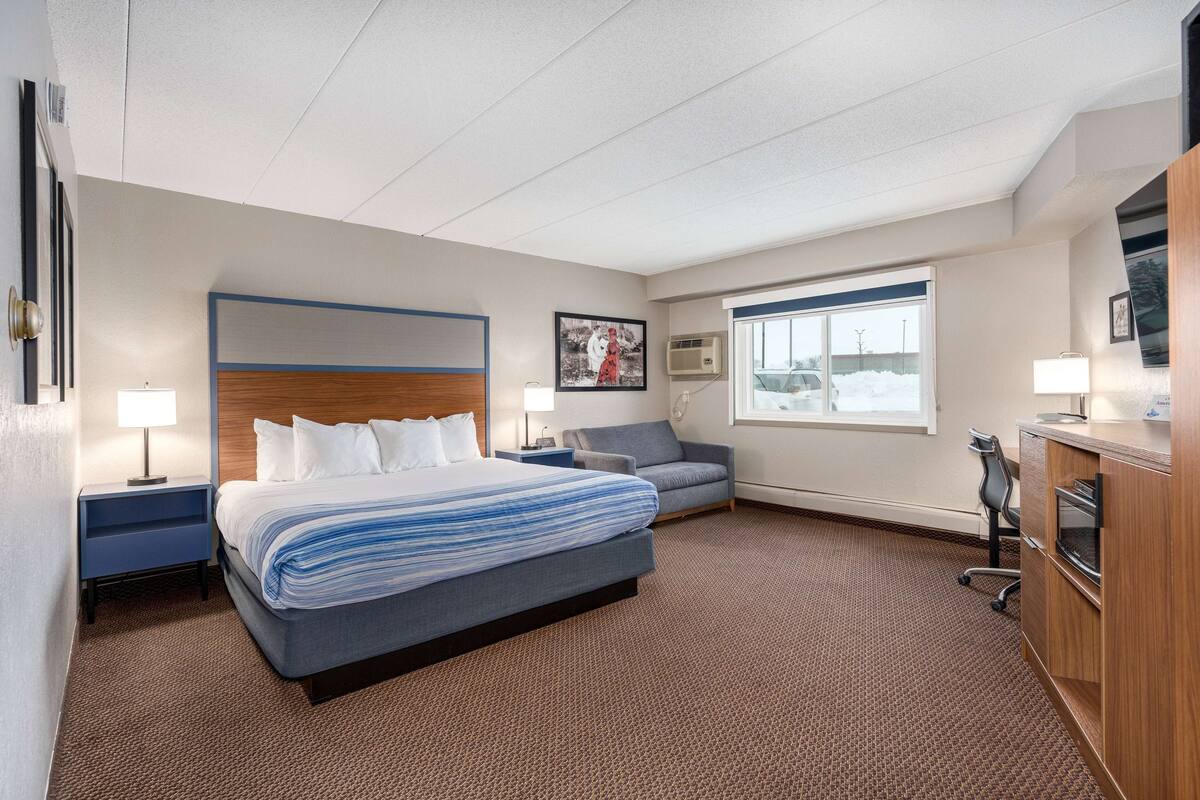 A hotel room with a bed, a desk, a chair, a TV, and a window.