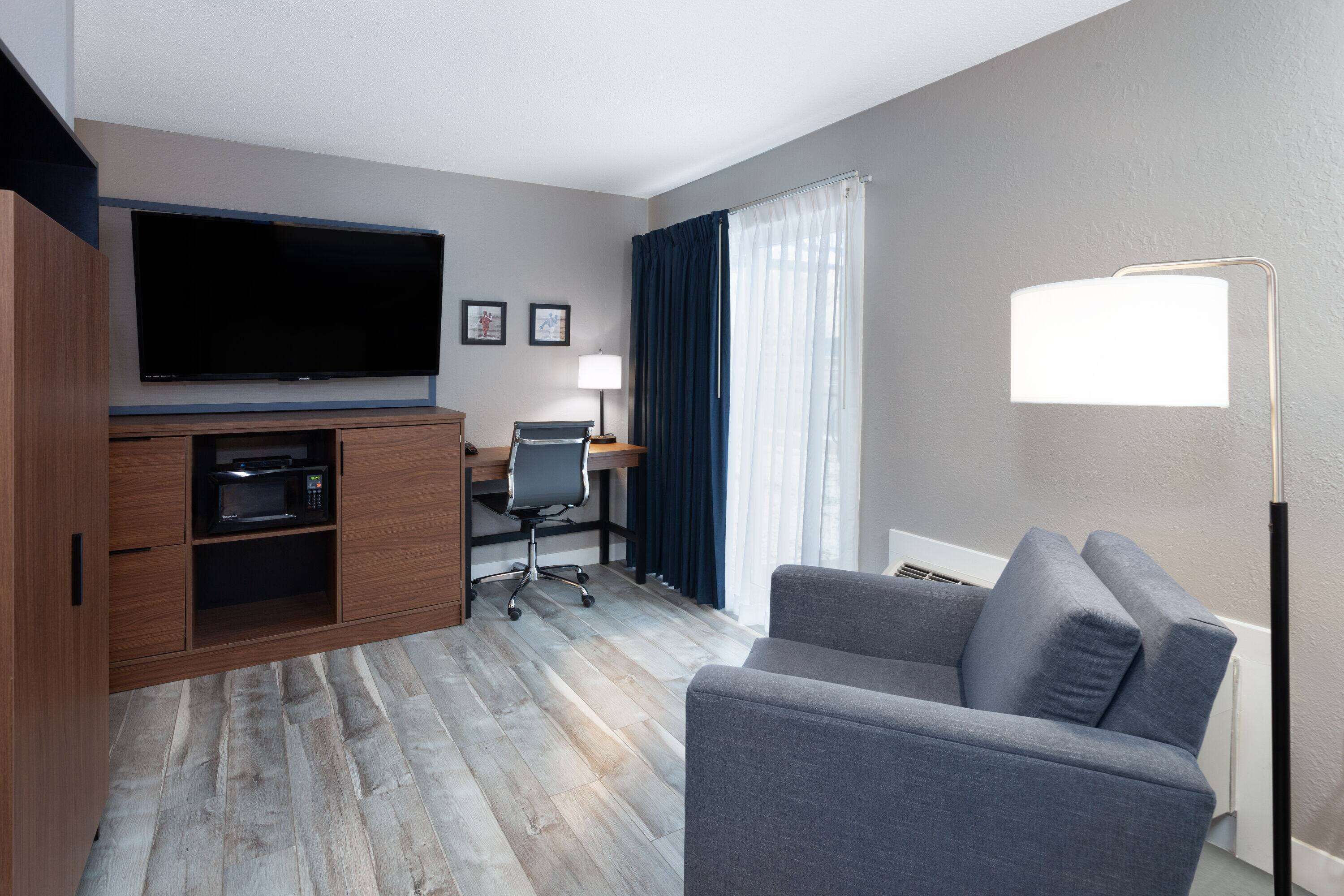 A modern hotel room with a flat-screen TV, a desk with a chair, a sofa, a lamp, and a microwave.