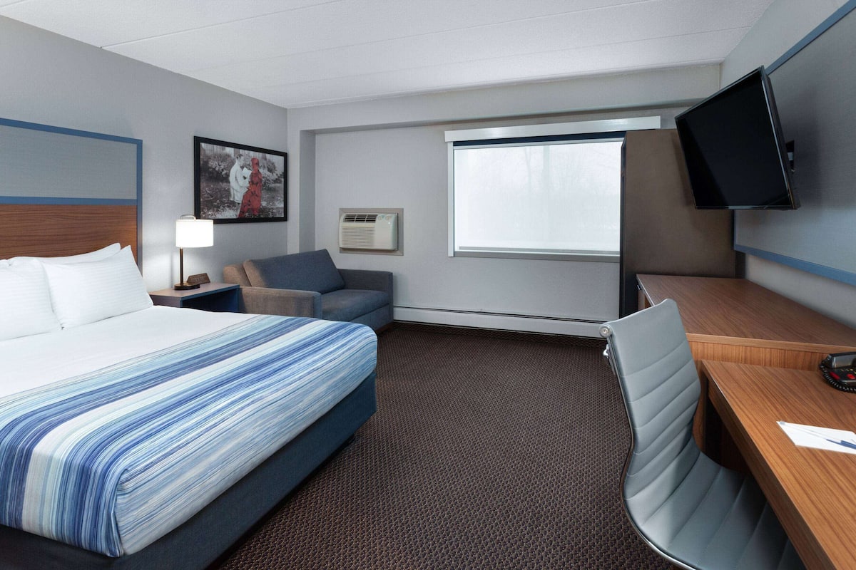 A hotel room with a bed, a desk, a chair, a television, a window, and a picture on the wall.