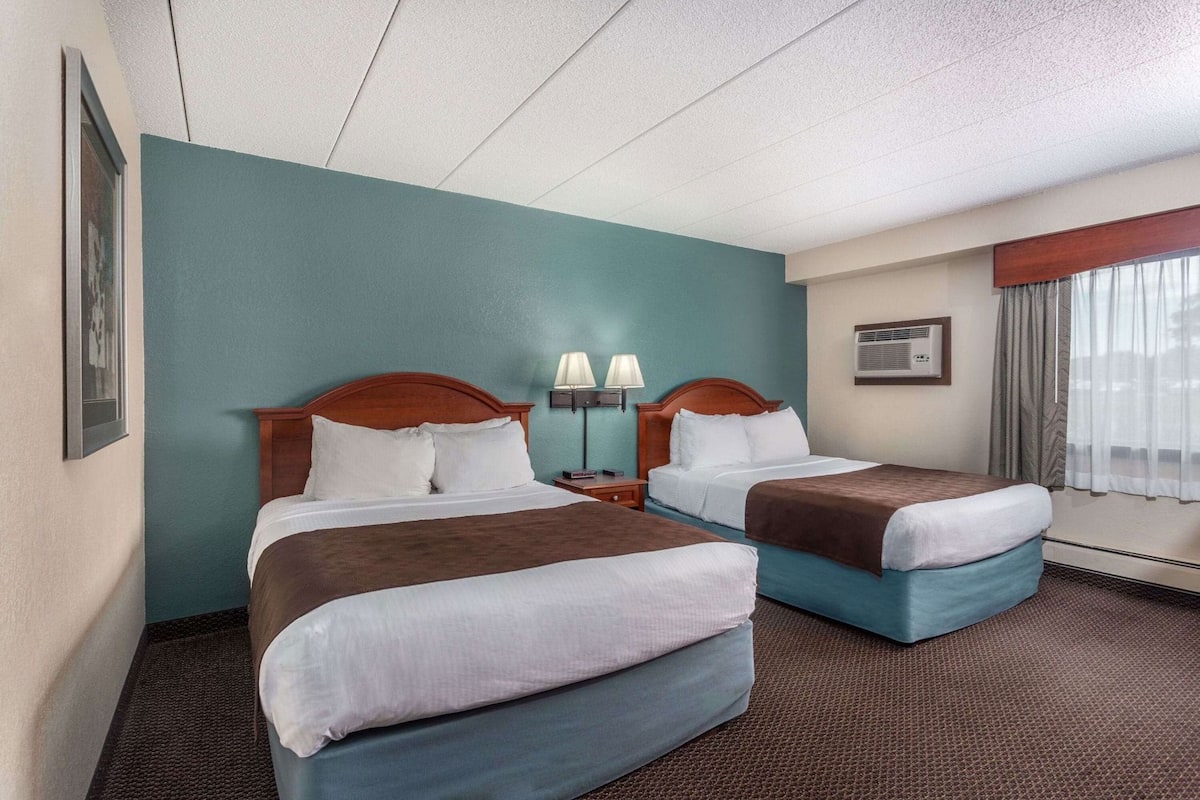 A hotel room with two beds, a nightstand with lamps, a framed picture on the wall, and an air conditioning unit.
