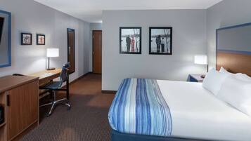 A hotel room with a bed, desk, chair, and two framed pictures on the wall.