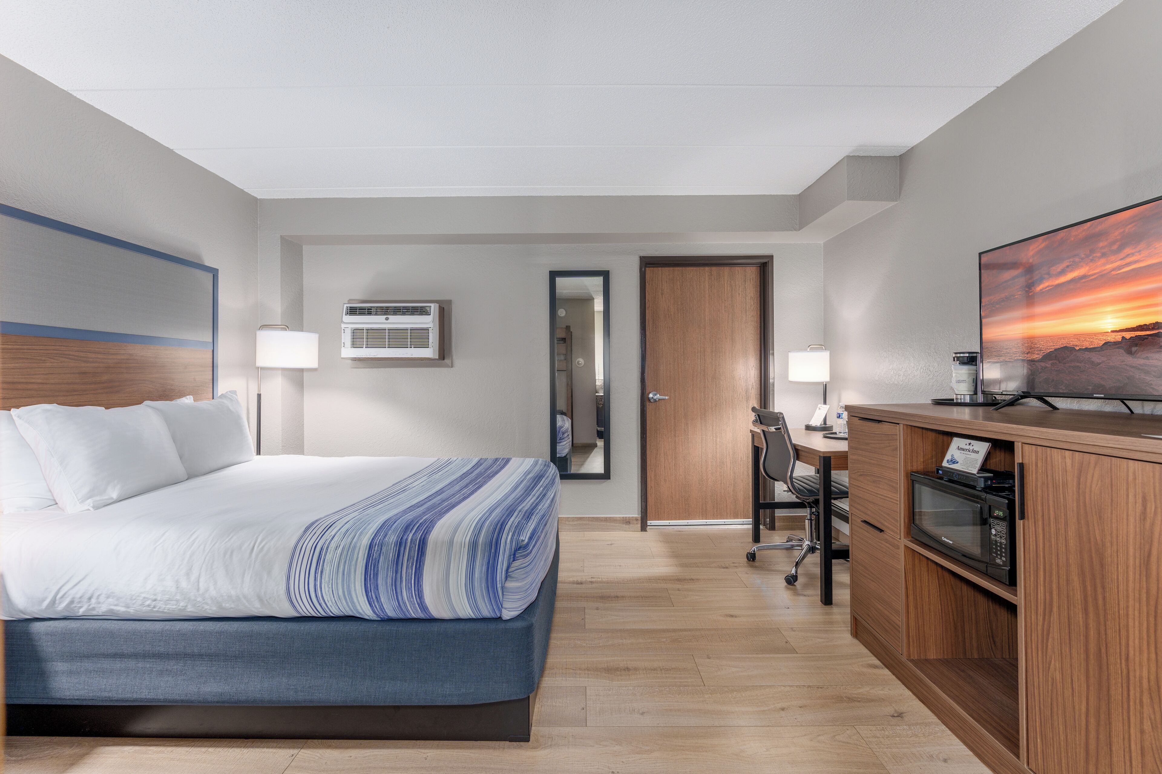 A hotel room with a bed, desk, microwave, and a large painting on the wall.