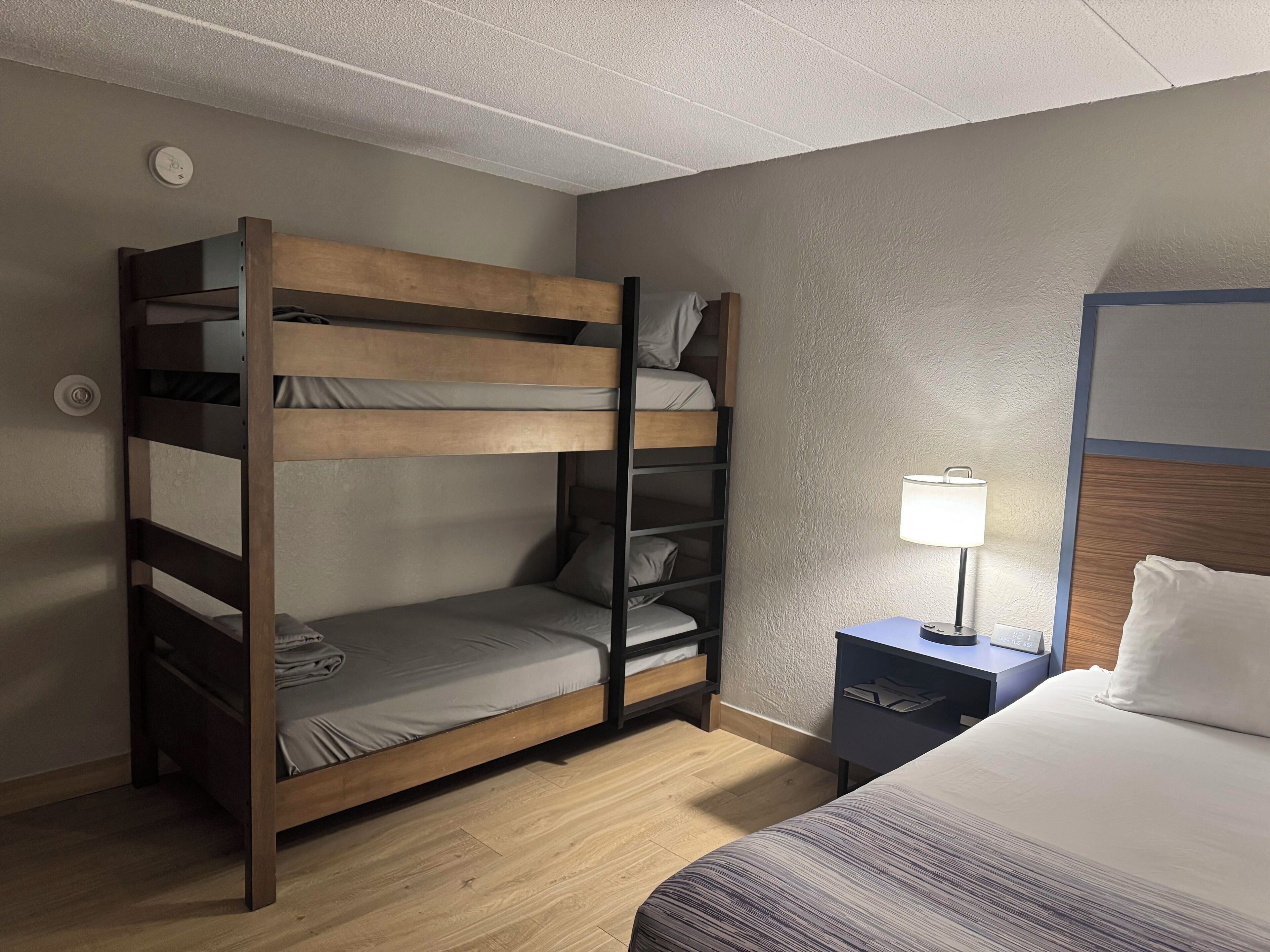 Una habitación de hotel con literas, un escritorio con lámpara y una cama separada.