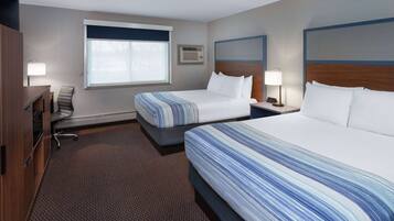A hotel room with two beds, a desk, a chair, a window, and a wall-mounted air conditioner.