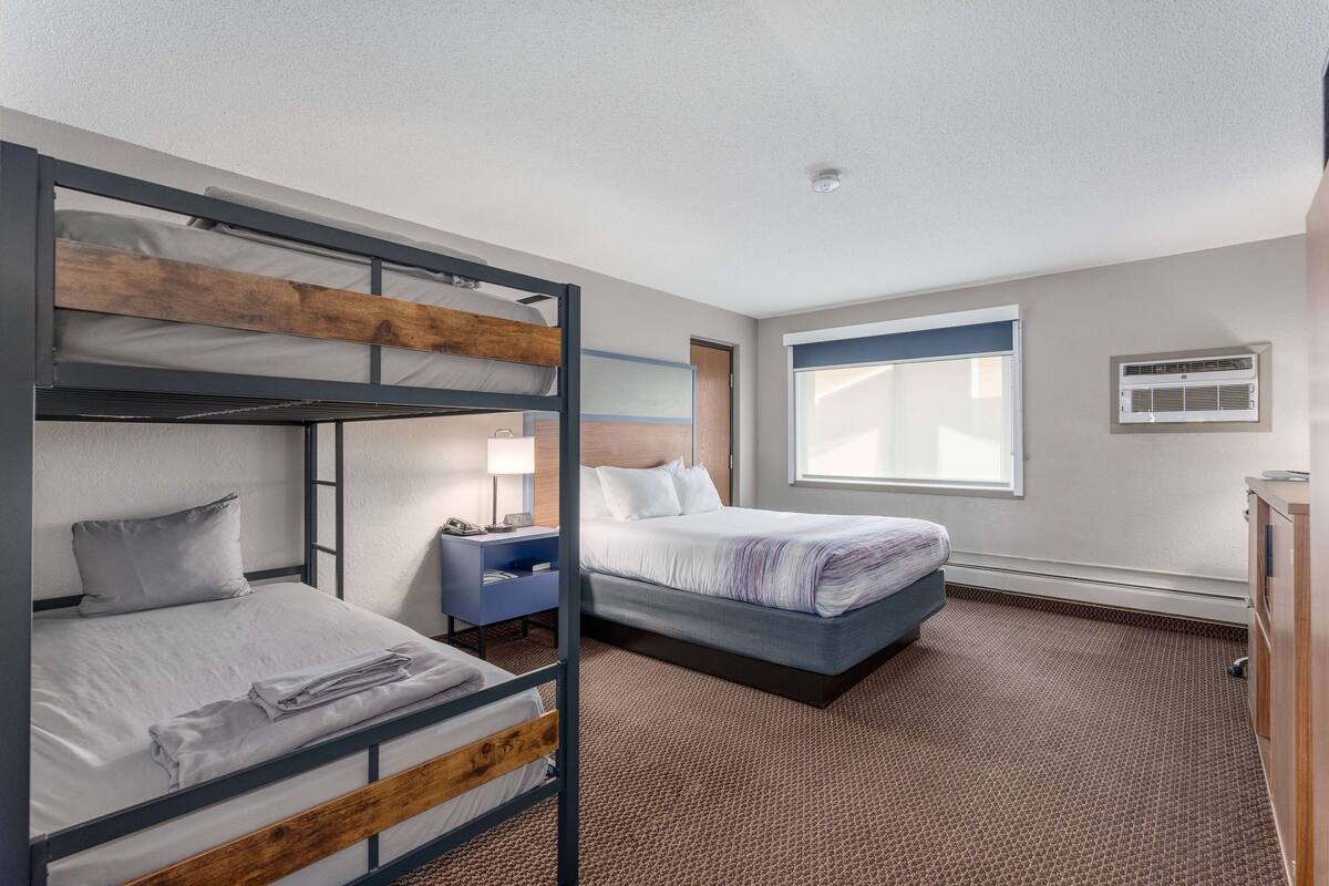 A hotel room with bunk beds, a desk, a lamp, and a window with blinds.