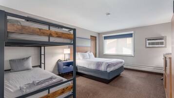 Een hotelkamer met stapelbedden, een bureau, een lamp en een raam met zonwering.