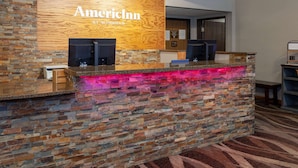 Una mesa de recepción con panel de madera y pared de piedra, que muestra el nombre 'AmericInn' y un letrero que indica 'By Wyndham'.