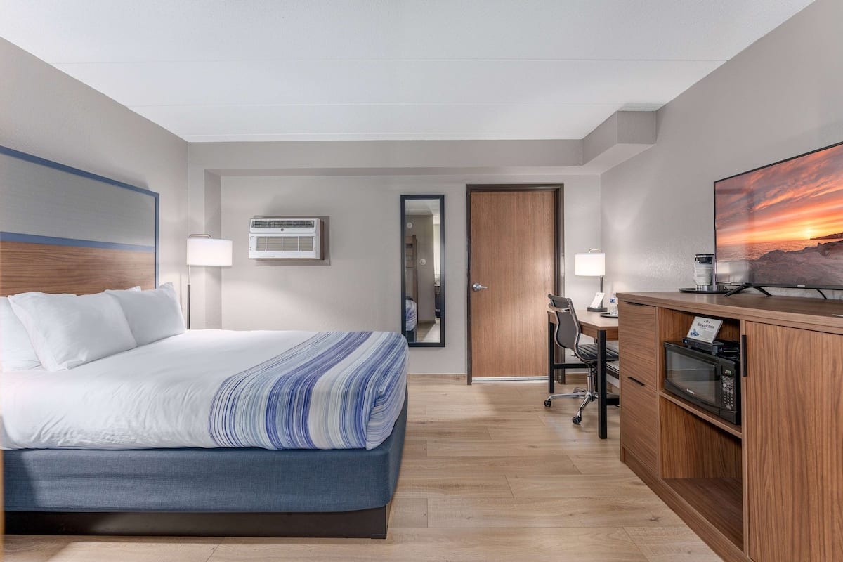 A hotel room with a bed, desk, microwave, and a large TV.