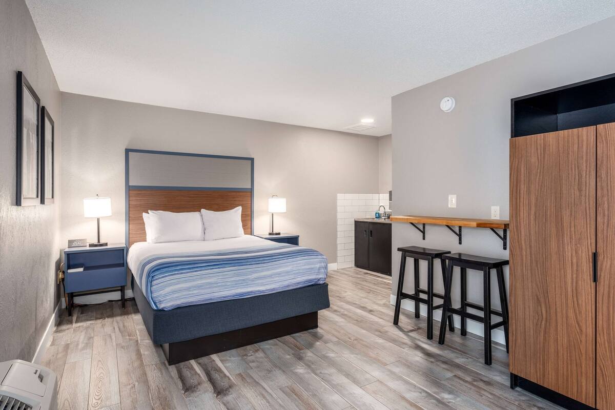 A modern hotel room with a bed, bedside tables, a desk, and a wardrobe.